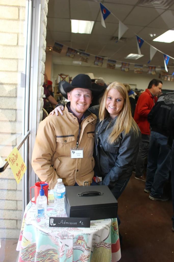 Smiling young man in black cowboy hat and woman at the admission table with a cash box and Admission $5 sign at the 2019 CCG show at Prescott Rodeo Grounds