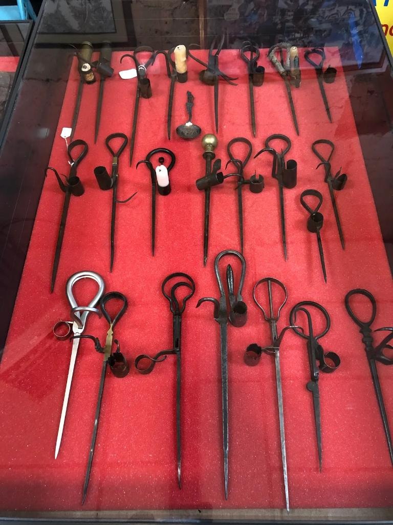 Glass display case packed with rows of antique iron scissors and candle snuffers with decorative handles laid out on red velvet