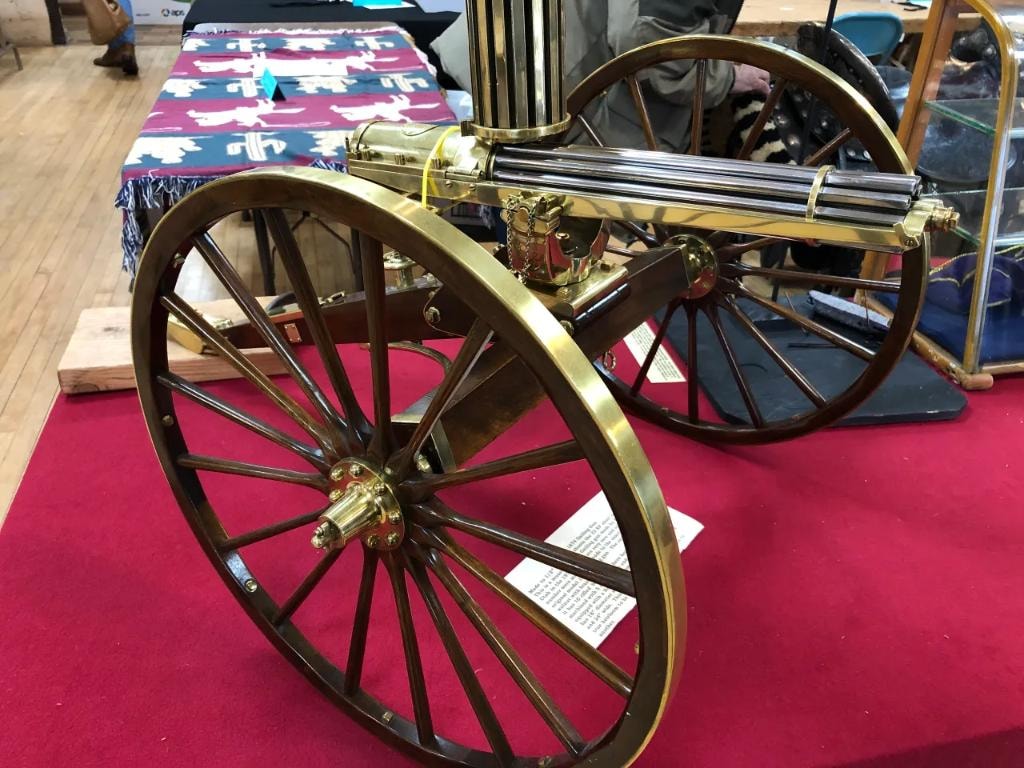 Antique brass and wood Gatling gun replica on a wheeled carriage displayed on red carpet at the 2020 CCG show at Prescott Rodeo Grounds