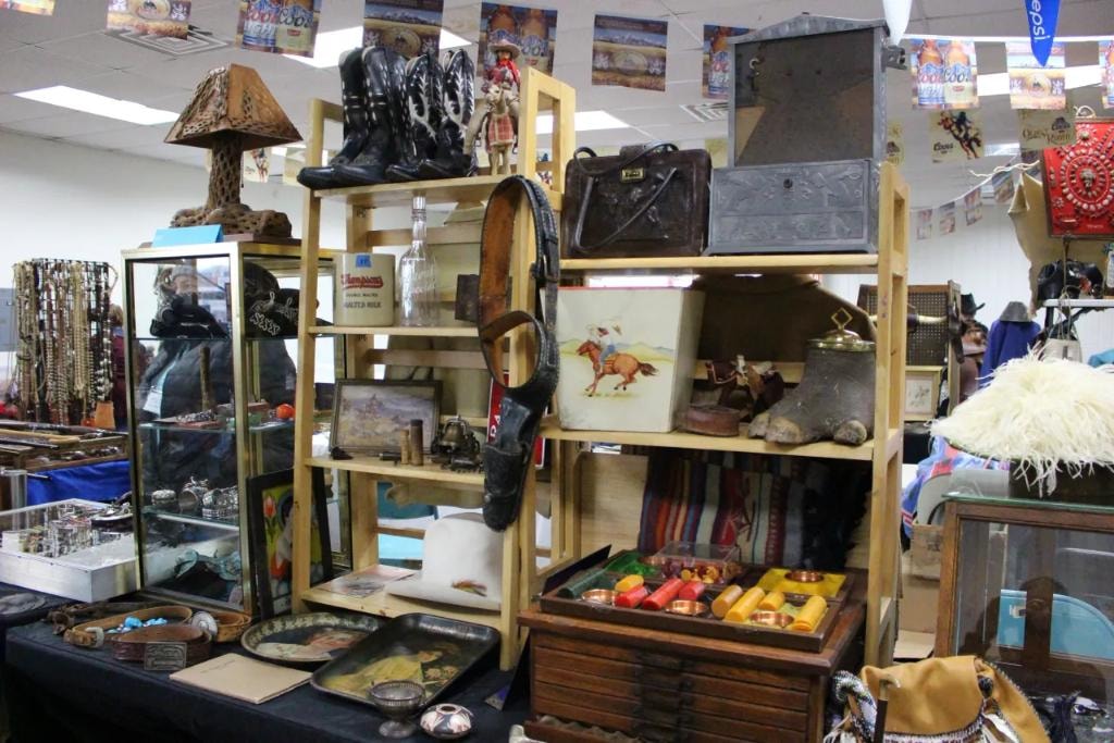 Vendor booth with wooden shelves packed with cowboy boots, leather bags, vintage tins, Bakelite jewelry, and western collectibles