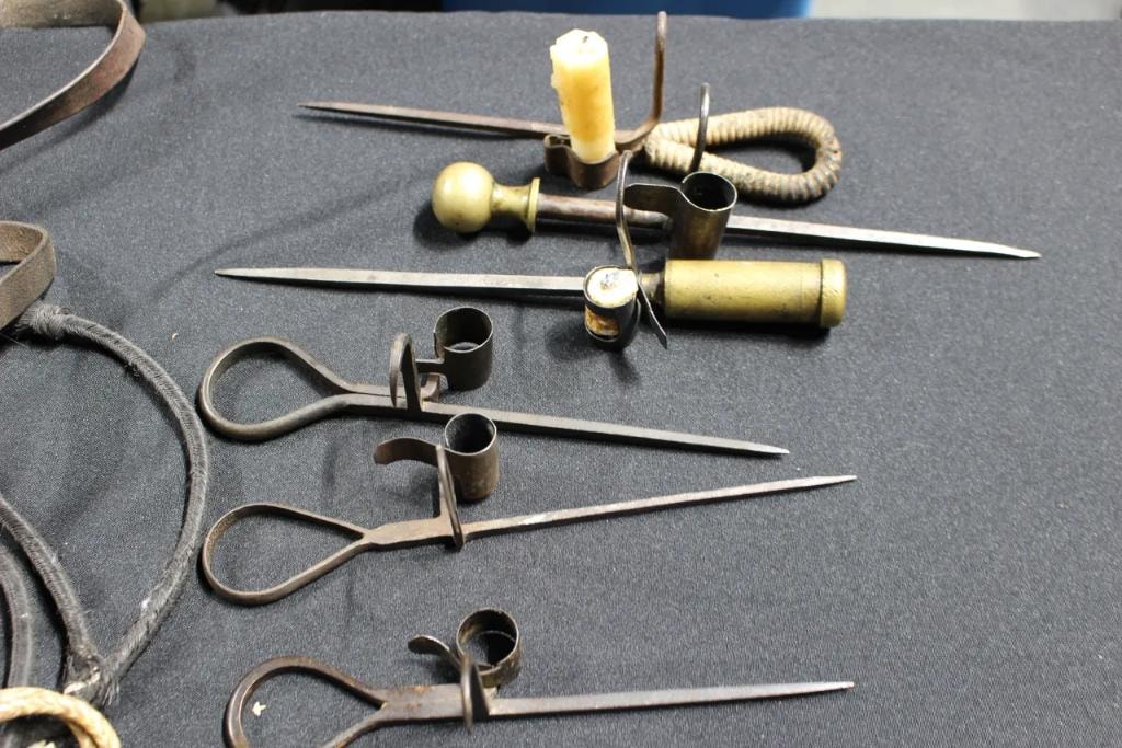 Antique iron candle holders, scissors, and spike tools displayed on a gray cloth table