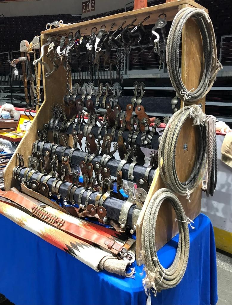 Large wooden display case packed with rows of antique western spurs and bits, with coiled lasso ropes on the side