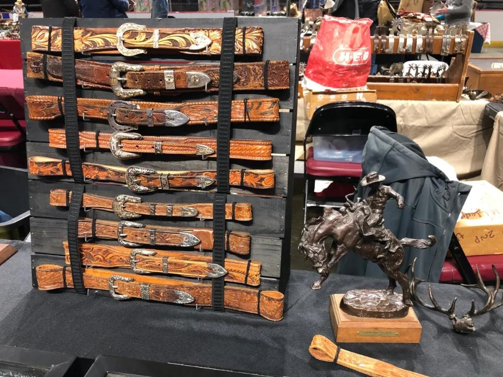 Display board of hand-tooled western leather belts with silver buckles alongside a bronze bucking bronco sculpture