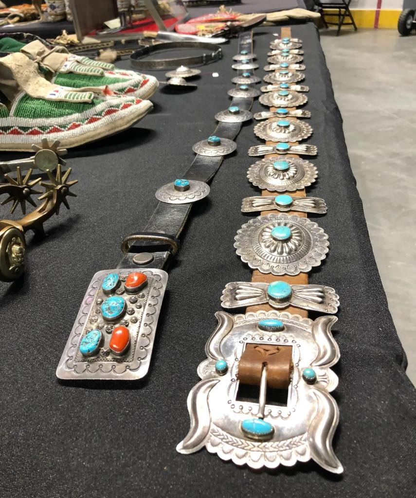 Full-length Navajo silver and turquoise concho belt laid out on a black table alongside beaded bags and spurs