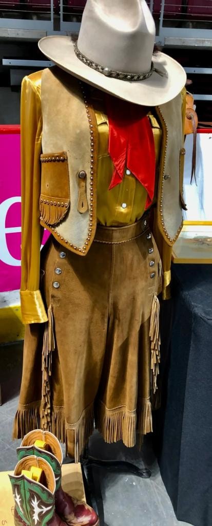 Fringed suede cowgirl outfit with studded vest, red scarf, and cowboy hat displayed on a mannequin