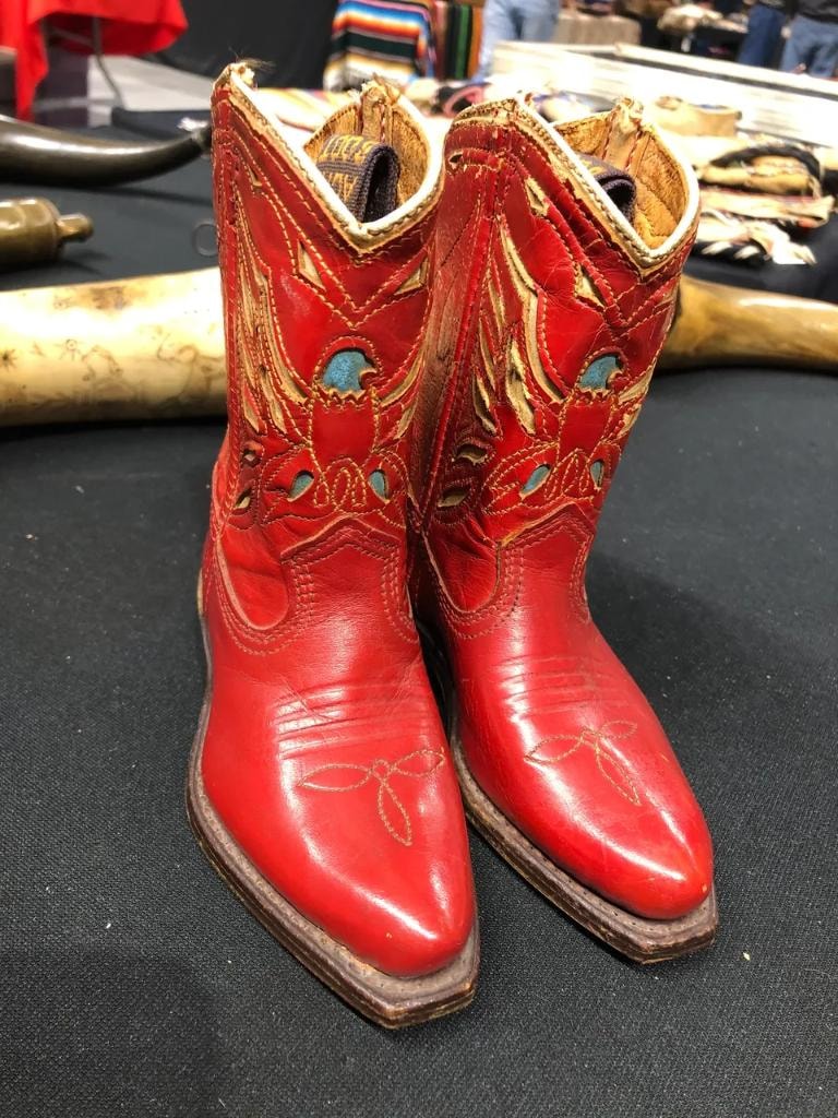Pair of vintage red and gold children's cowboy boots with turquoise inlay cutouts on a black table