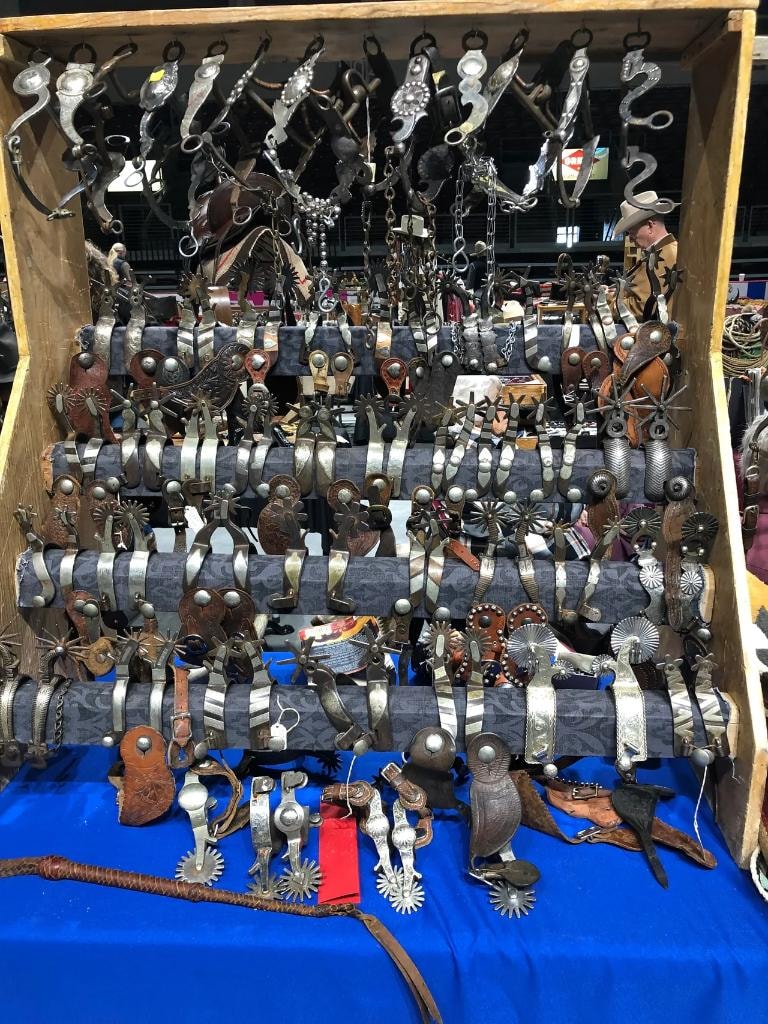 Massive wooden display board packed with hundreds of antique western spurs hanging and laid out on a blue table