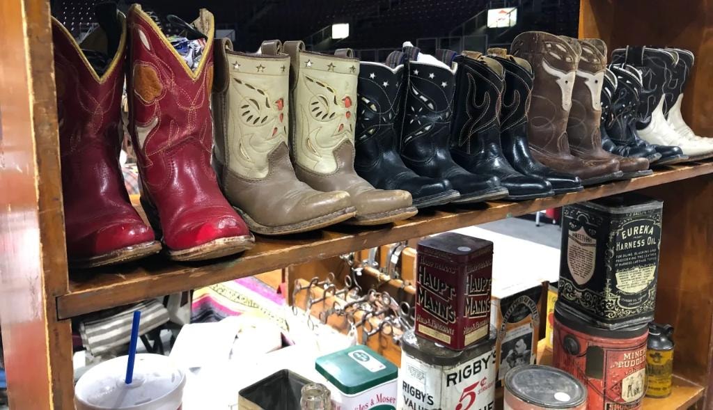 Row of vintage cowboy boots in red, cream, black, and brown displayed on a wooden shelf with antique tins below