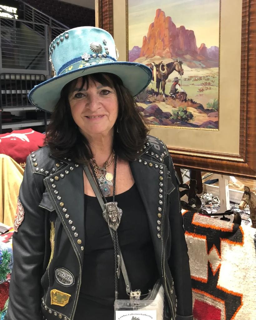 Smiling woman vendor in a turquoise hat with silver conchos and a studded leather jacket at her CCG booth