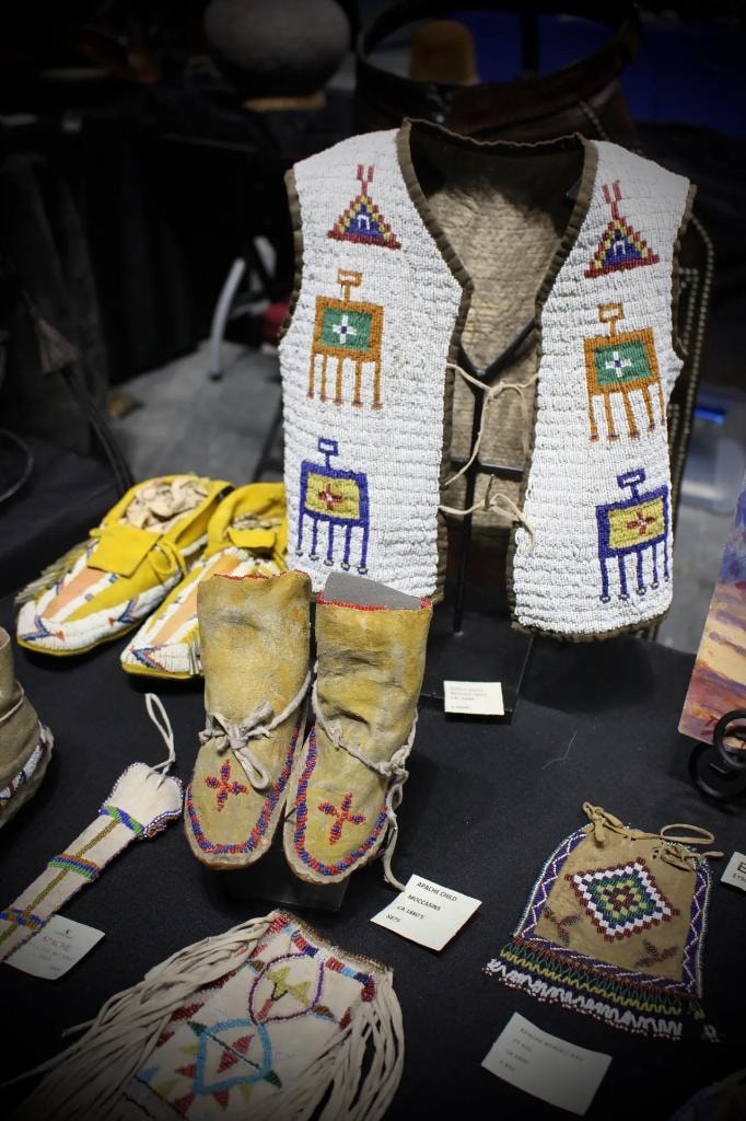 Native American beaded vest, Apache child moccasins, and beaded pouches displayed on black table