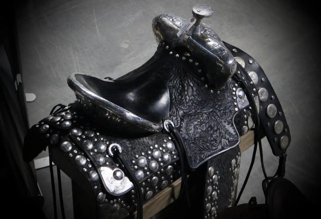 Ornate black leather western saddle covered in silver studs and engraved silver conchos displayed on a stand