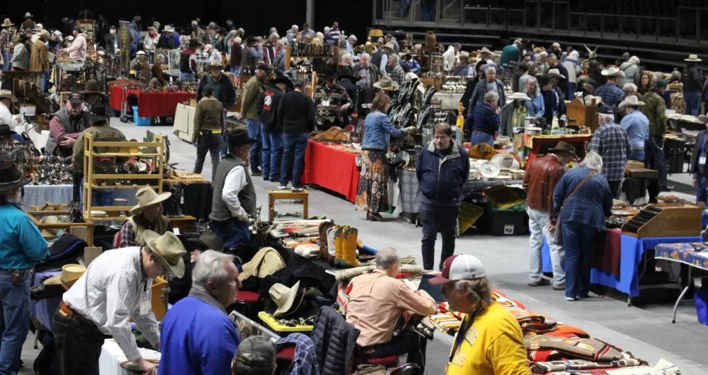 Crowd of collectors in cowboy hats browsing tables loaded with western gear, boots, and Native American textiles