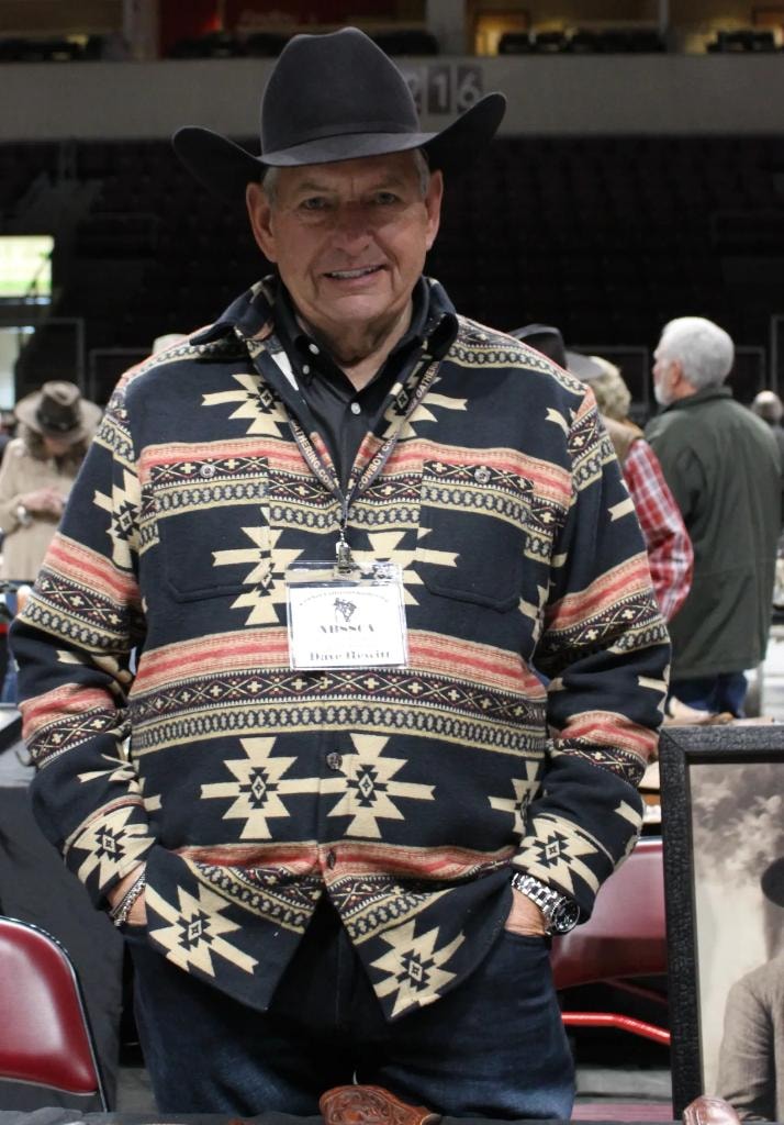 Man wearing a black and tan Aztec-pattern jacket with CCG badge standing at his vendor booth