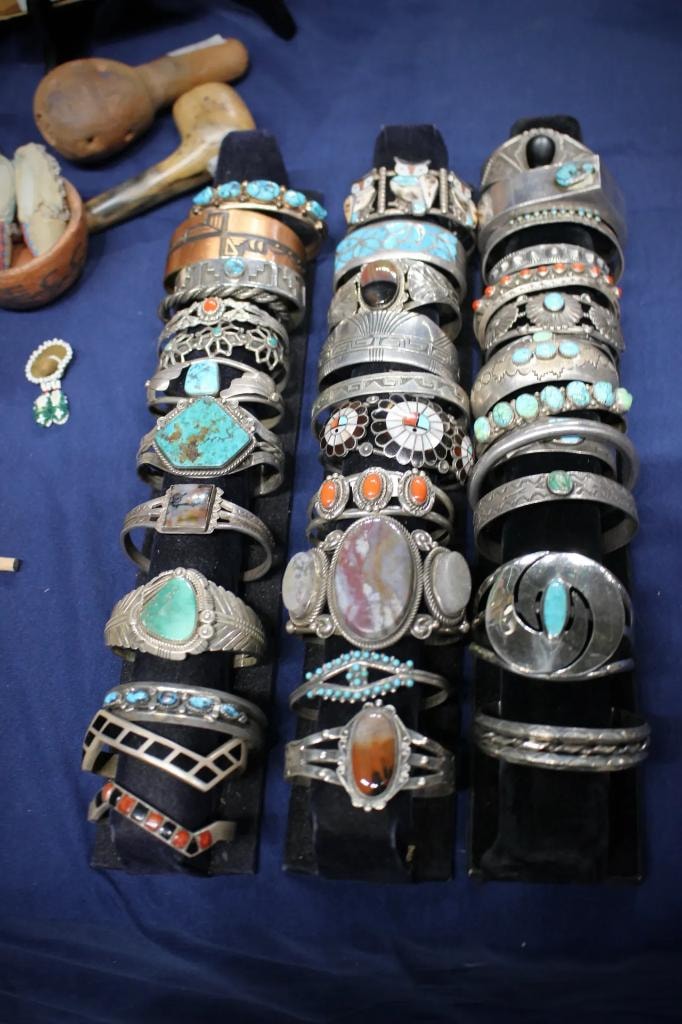 Three tall stands stacked with antique Native American silver and turquoise cuff bracelets on a blue velvet table