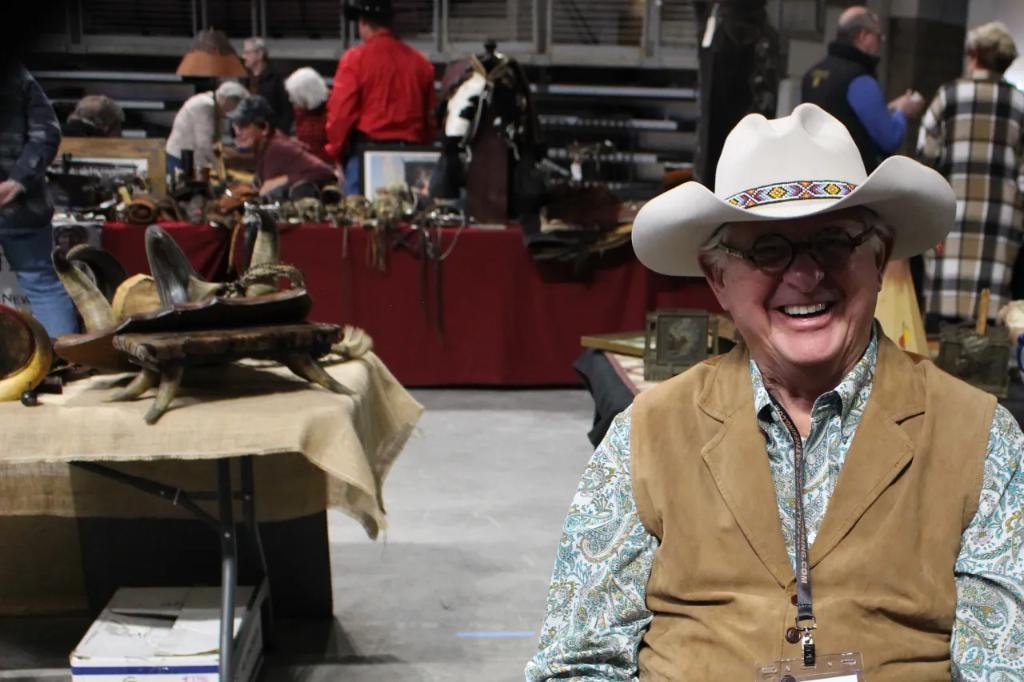 Laughing man in white cowboy hat with beaded band standing at his vendor booth