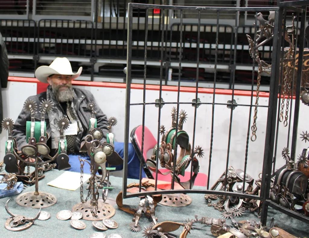 Cowboy vendor seated behind a large display of antique spurs and western hardware