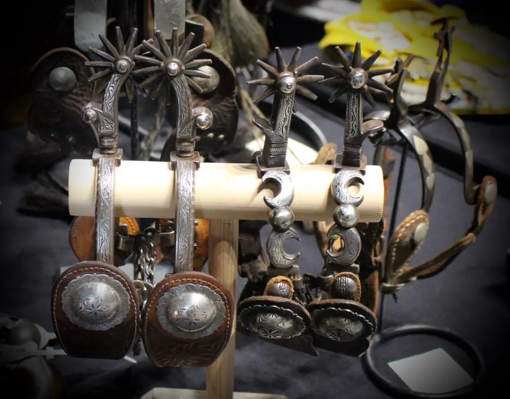 Decorative antique western spurs with concho straps displayed on a wooden stand
