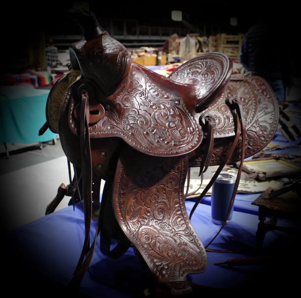 Ornately hand-tooled floral leather western saddle at a vendor booth