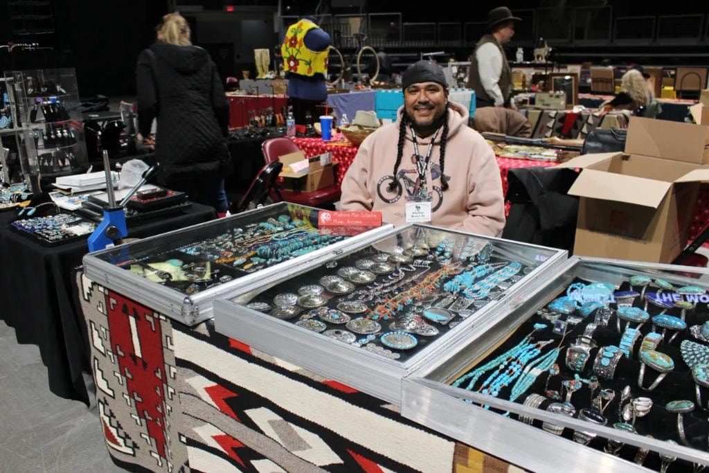 Native American vendor smiling behind a glass case full of turquoise and silver jewelry