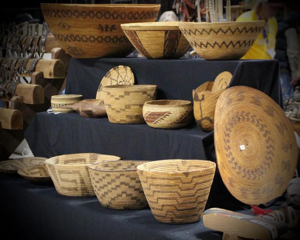 Collection of Native American woven baskets with geometric patterns displayed on tiered black cloth steps