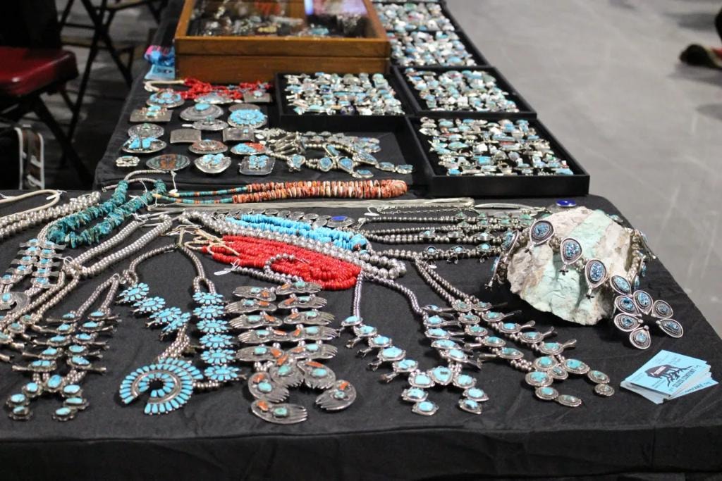 Turquoise squash blossom necklaces and silver jewelry on black table