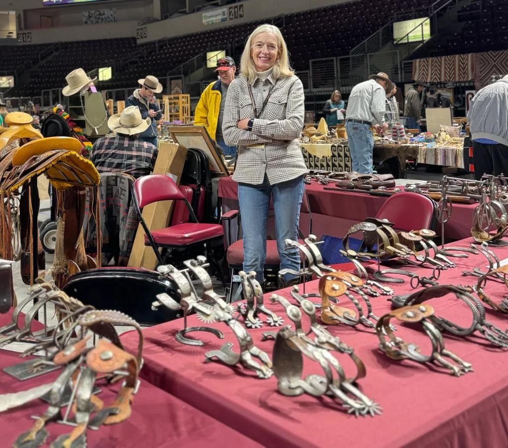 Woman standing at table full of antique western spurs at the show